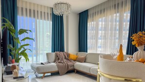 A modern living room with a sectional sofa, a round coffee table, a chandelier, and a large window with curtains. - Qoople Eхсellence A-49 neue Wohnung am Meer by Interhome (Alanya)