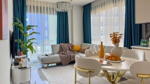 A modern living room with a sofa, dining table, and chairs. There is a chandelier, a plant, and a vase with flowers. - Qoople Eхсellence A-49 neue Wohnung am Meer by Interhome (Alanya)