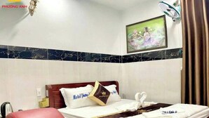 Una camera d'albergo con un letto, una sedia rossa, una ventola a muro e un quadro appeso.
