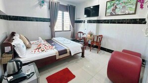 Una camera d'albergo con un letto, una scrivania con il telefono, una sedia rossa, un tavolino con un vaso e una TV appesa al muro.