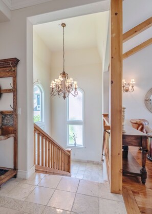 A spacious interior with a grand staircase, a chandelier, and a view of the outdoors. - Lake Arrowhead Waterfront Retreat | Game Room (Lake Arrowhead)