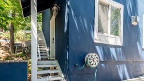 Une maison bleue avec une porte blanche, une fenêtre avec des stores, un porche avec une balustrade blanche et un tuyau d’arrosage raccordé à la maison.