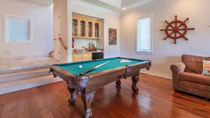 Une table de billard dans une pièce dont le sol est recouvert de parquet, avec un meuble en bois et une décoration murale représentant un gouvernail de navire.