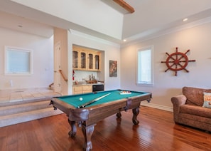 Une table de billard dans une pièce dont le sol est recouvert de parquet, avec un meuble en bois et une décoration murale représentant un gouvernail de navire.