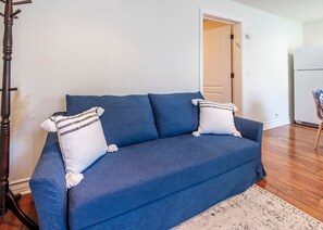 A blue sofa with two pillows, a white rug, and a wooden floor. - Lake Arrowhead Waterfront Retreat | Game Room (Lake Arrowhead)