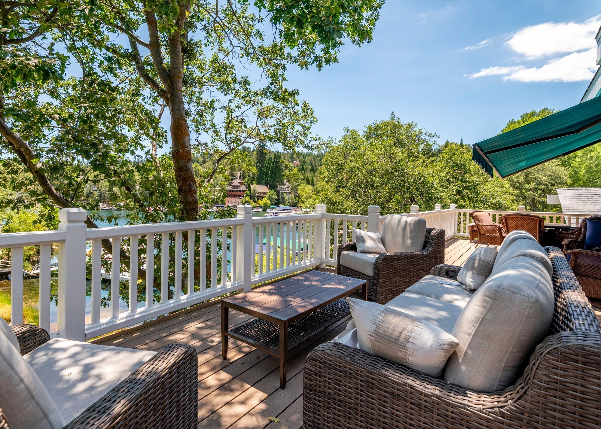 Une terrasse dotée de meubles en osier, d’une balustrade blanche et offrant une vue sur un lac et des bâtiments en arrière-plan.