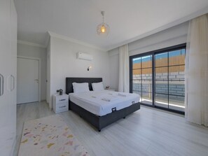 Un dormitorio moderno con una cama grande, una mesita de noche, una lámpara de techo y vistas al exterior a través de un ventanal corredero.