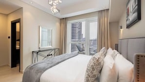 A modern hotel room with a large bed, a desk, and a view of a cityscape through the window. - Vogue | Mon Reve Downtown near Dubai Mall | Burj Khalifa (Dubai)