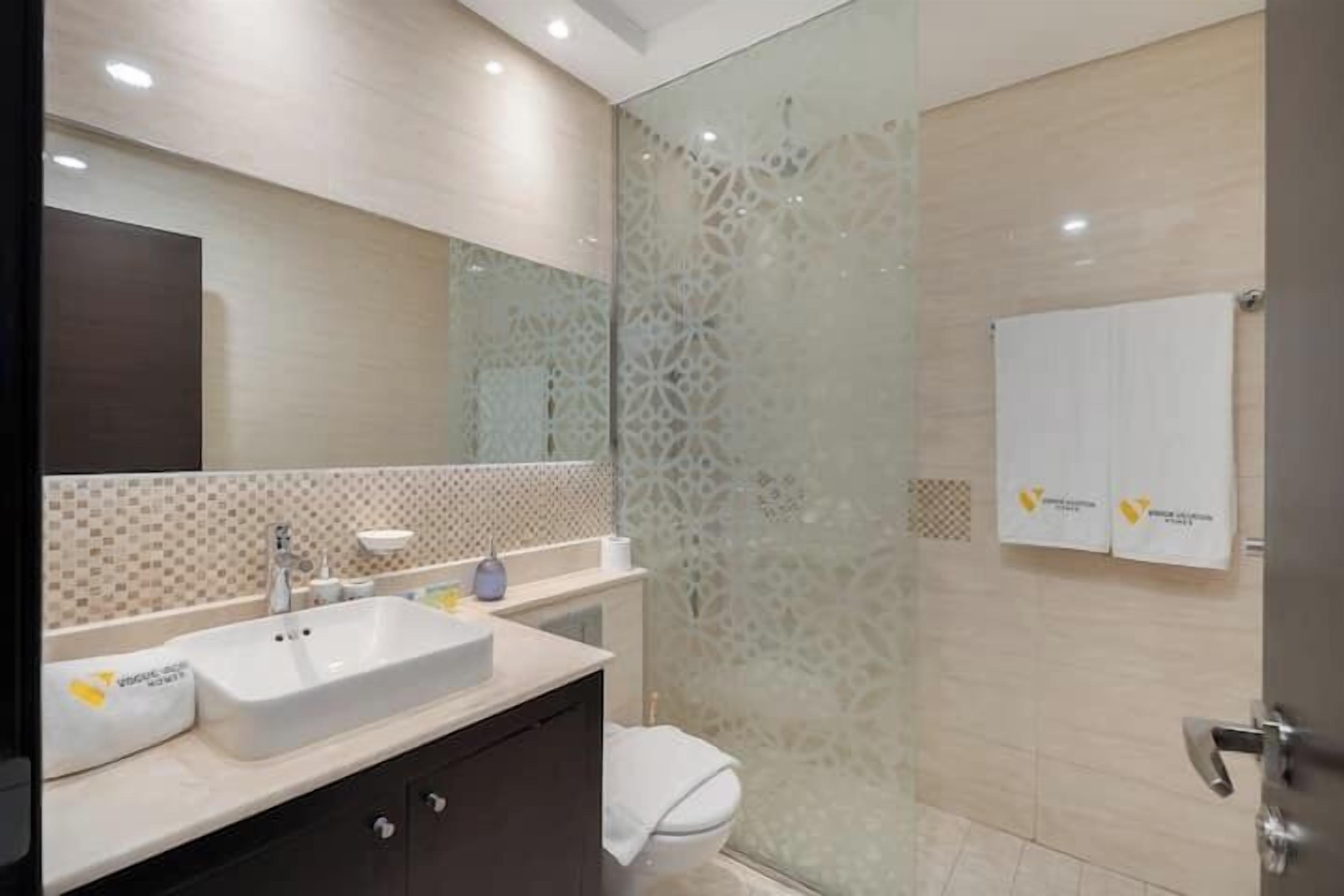 A modern bathroom with a large mirror, a white sink, and a toilet.