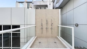 A modern outdoor shower area with three showerheads, glass railings, and a tiled floor. - Vogue | Mon Reve Downtown near Dubai Mall | Burj Khalifa (Dubai)