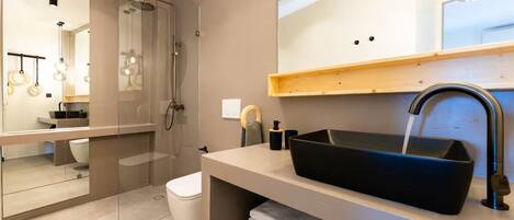 A modern bathroom with a glass-enclosed shower, a black sink, and a wooden shelf with towels.