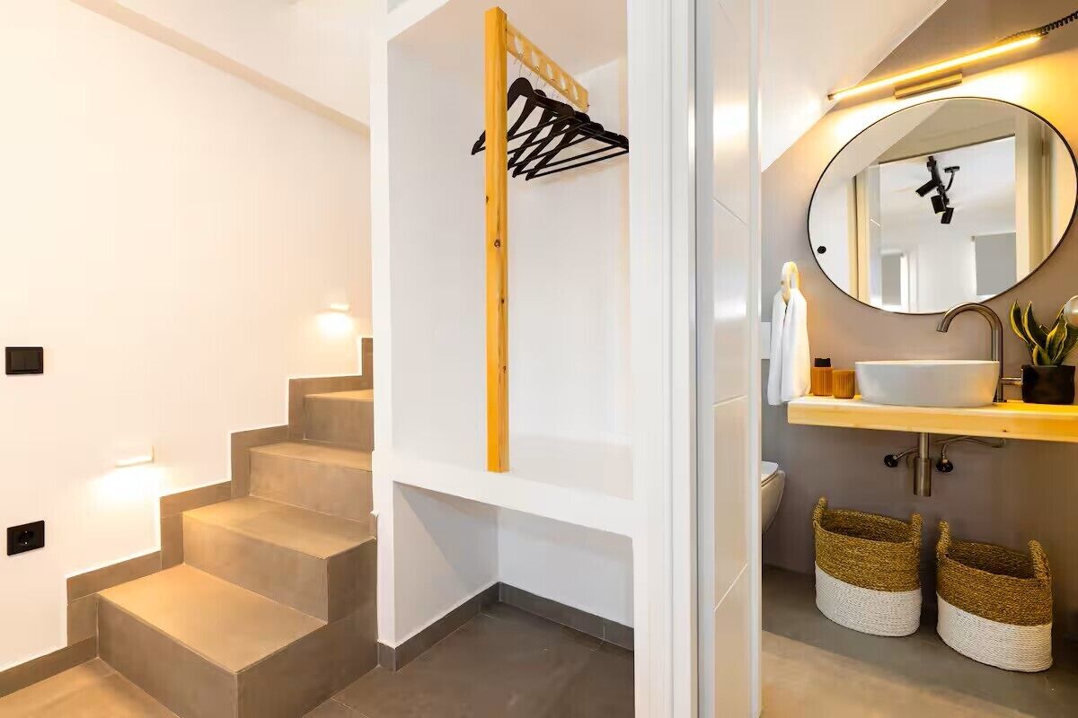 Une salle de bain moderne avec un miroir rond, un lavabo blanc et un porte-serviettes en bois.