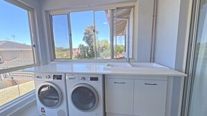A compact laundry room with a washing machine and dryer, a sink, and a window offering a view of the neighborhood. - Room-executive Style Stay, Fast Wi-fi, p (Perth)