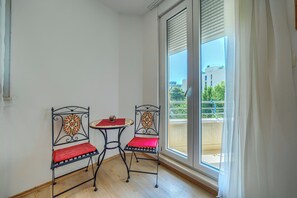 A room with two metal chairs and a small table, a sliding glass door to an outdoor balcony, and a view of buildings and greenery outside. - A Comfortable apt w Balcony, 4 min Walk to Beach (Split)