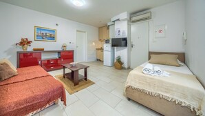 Una habitación de hotel pequeña con una cama, un escritorio, una kitchenette y un armario rojo.