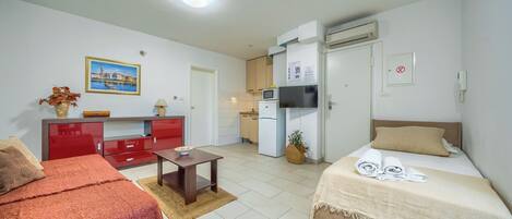 Une chambre d’hôtel de taille réduite, comprenant un lit, un petit bureau, une kitchenette et un placard rouge.