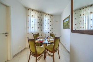 A dining area with a round table set for four, surrounded by green upholstered chairs. - A Comfortable apt w Balcony, 4 min Walk to Beach (Split)