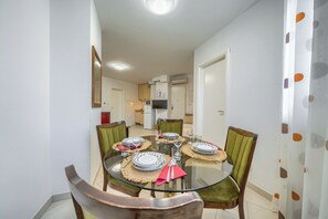 A dining area with a glass table, four chairs, and a kitchen in the background. - A Comfortable apt w Balcony, 4 min Walk to Beach (Split)
