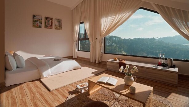 A modern bedroom with a large window, a sofa, a coffee table, and artwork on the wall. - Yen Stay and Coffee (Xuan Huong - Da Lat)