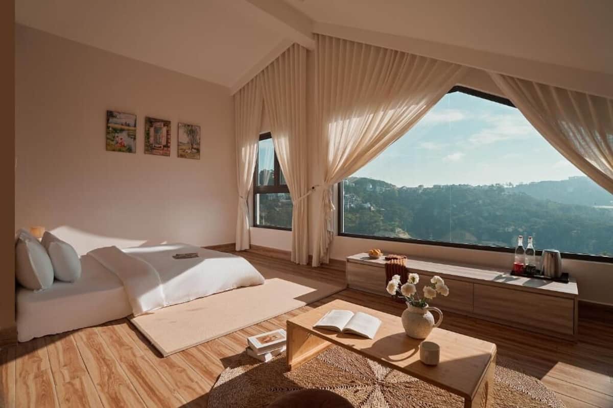 Une chambre à coucher moderne avec une grande fenêtre, un canapé, une table basse et des œuvres d’art accrochées au mur.