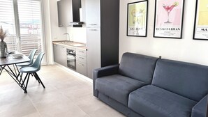 Een moderne keuken met grijze kastjes, een ingebouwde oven en een eethoek met een tafel en stoelen. Er hangen ingelijste foto's aan de muur.