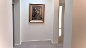Een gang met een lijstwerkschilderij van bloemen aan de muur, een dakraam en een deur aan de rechterkant.