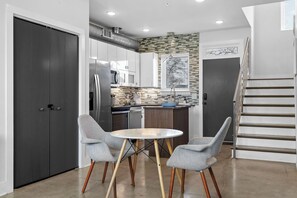 A modern kitchen with a dining area, featuring a round table and two chairs, a staircase, and a view of the outside. - New! The Skyline Stage / 10 min to Broadway! (Nashville)