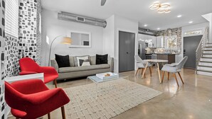 Ein modernes Wohnzimmer mit einem roten Sessel, einem grauen Sofa und einem Essbereich mit Tisch und Stühlen.