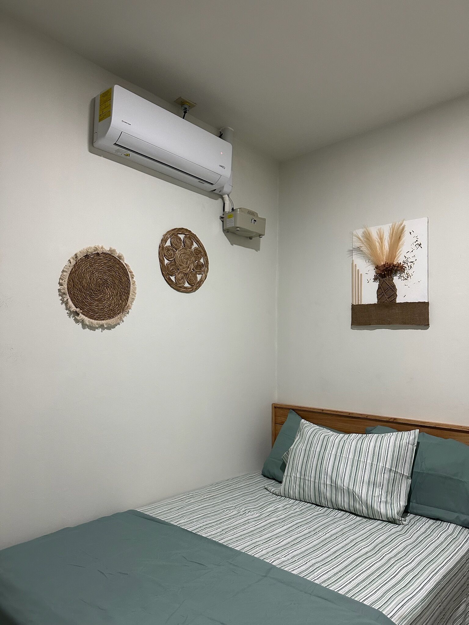 A bedroom with a bed, a wall-mounted air conditioner, and two wall decorations.