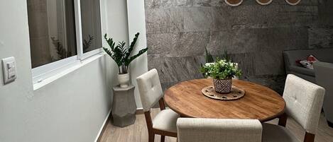 Un coin repas comprenant une table ronde en bois, quatre chaises, un luminaire suspendu en fibres tressées et un mur en pierre orné de motifs circulaires.