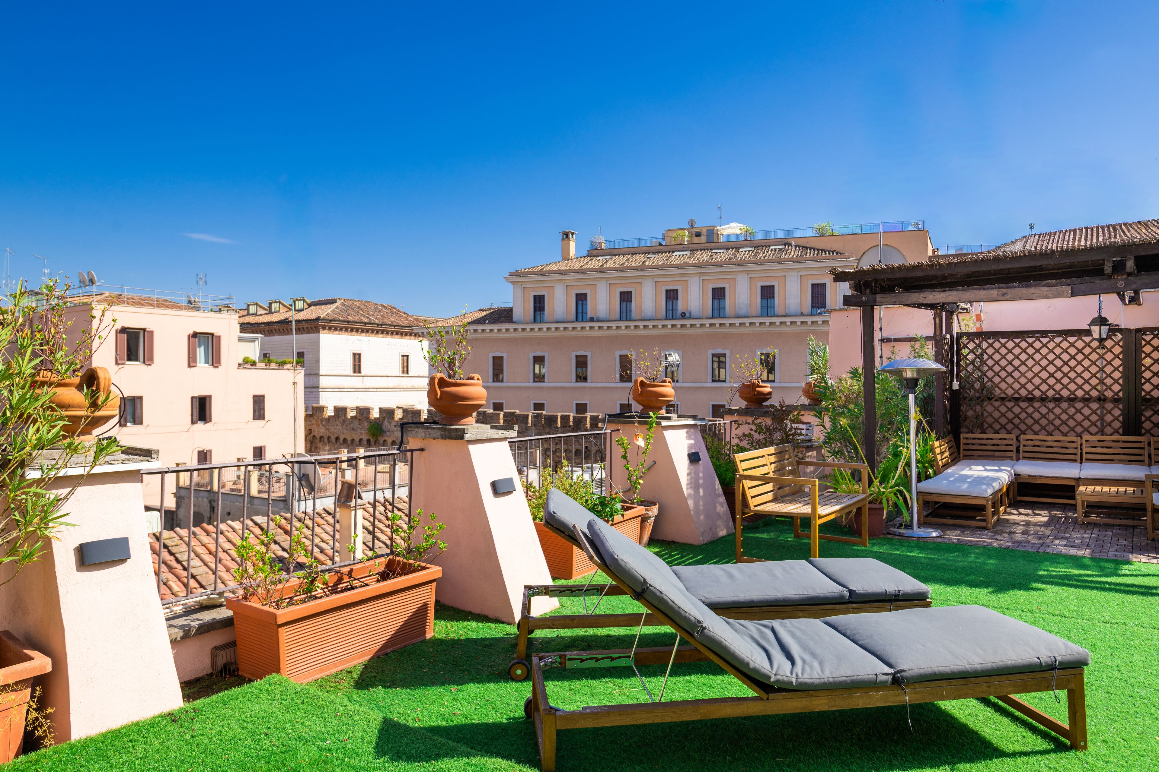 Una terraza en la azotea con área de descanso, plantas en macetas y edificios tradicionales al fondo.