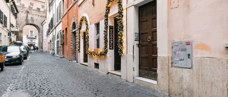 A cobblestone street with buildings, a sign for "Hotel Arte Sacra," and a brown door.