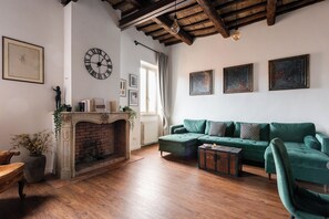 Un salon avec une cheminée, un canapé vert, un plancher en bois et une horloge au mur.