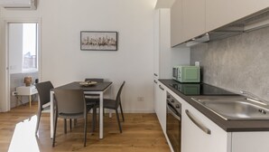 Eine moderne Küche mit weißen Schränken, einer Edelstahlspüle und einer Mikrowelle. Ein Essbereich mit Tisch und Stühlen sowie ein Fenster, das für natürliches Licht sorgt.