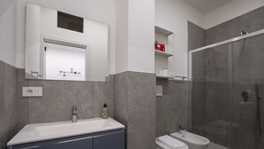 Ein modernes Badezimmer mit einem großen Spiegel, einem Waschbecken, einem Bidet und einer Duschkabine.