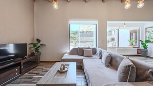 A modern living room with a flat-screen TV, a sofa, a coffee table, and a large window offering a view of the outdoors. - Altura Villa,Private Pool , one storey , for Up to 7 geusts (Saitoures)