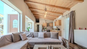 A modern living room with a wooden ceiling, a sofa, a coffee table, and a kitchen in the background. - Altura Villa,Private Pool , one storey , for Up to 7 geusts (Saitoures)