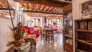 Un interior rústico con vigas de madera a la vista, una zona de comedor con mesa y sillas, un sofá rojo y una estantería.