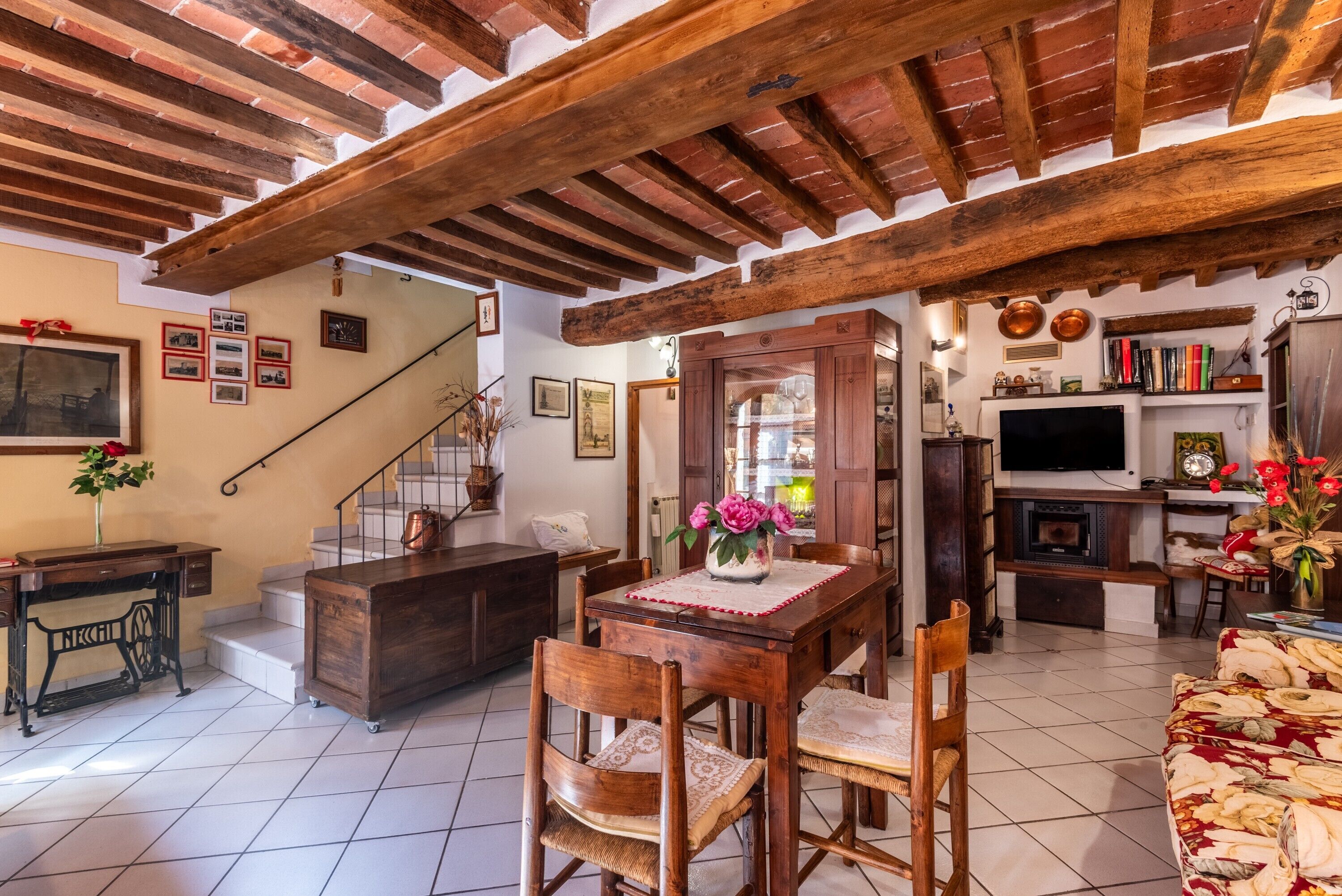 Un intérieur rustique avec des poutres apparentes, un coin repas avec une table et des chaises en bois, un escalier et un salon avec un canapé et une télévision.