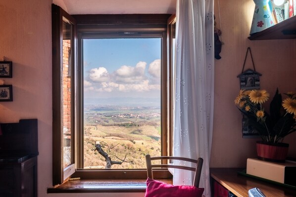 Ein Zimmer mit großem Fenster, einem Sessel, einem Holztisch und einem Regal mit Dekoration.
