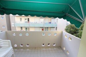 Un balcón con toldo verde, piso de baldosas y varios orificios circulares en la pared.