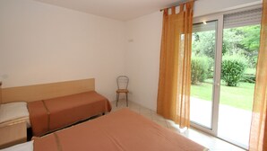 Habitación de hotel con dos camas, una silla y puerta corrediza de cristal a un jardín.
