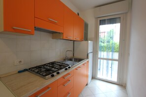 Eine Küche mit orangefarbenen Schränken, einem Gasherd und einem Fenster mit Blick auf Grünflächen.