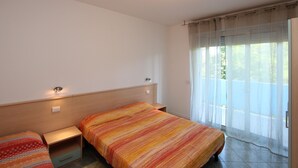 Een hotelkamer met twee bedden, een houten hoofdeinde, een klein nachtkastje en een raam met dunne gordijnen.