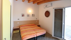 A bedroom with a bed, a nightstand, a wall-mounted light, a window with a view, and a door with a screen. - Duplex 100mt from the beach (Bibione Pineda)
