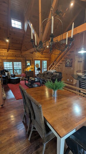 A spacious log cabin interior with a large dining table, wicker chairs, a fireplace, and a cozy living area with a sofa and cushions. - Anything's Pawsible – Game Room & Cozy Big Canoe Escape (Jasper)