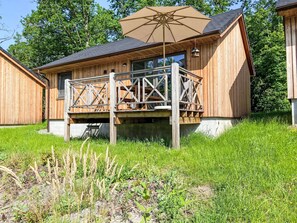 En stuga byggd av trä med en balkong, ett stort parasoll och utsikt över den omgivande naturen.