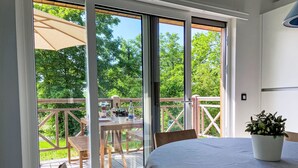 Ein Zimmer mit einer Schiebetür zu einer Terrassenanlage, einem runden Tisch mit Tischdecke und einer Topfpflanze auf dem Boden.
