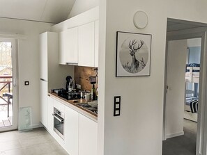 A modern kitchen with white cabinets, a stove, and a sink. There's a framed deer picture on the wall and a door leading to a room with bunk beds. - Chalet Wadi by Interhome (Heure)