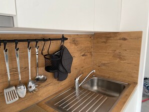 A kitchen with a wooden backsplash, stainless steel sink, and utensils hanging on a rack. - Chalet Wadi by Interhome (Heure)